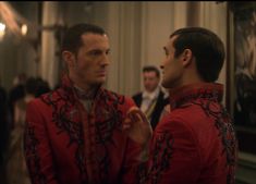 two men standing next to each other in front of a mirror wearing red and black clothing