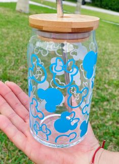 a hand holding a glass with mickey mouse decals on it and a straw in the lid