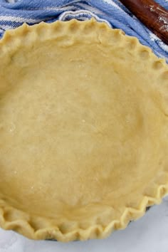 an uncooked pie crust on top of a blue and white towel next to a rolling pin