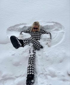 a woman laying in the snow with her legs spread out and wearing black and white checkered pants