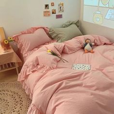 a bed with pink sheets and pillows in a room next to a small wooden table