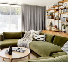 a living room filled with green couches next to a wooden table and bookshelves