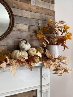 a mantel with pumpkins and leaves on it in front of a mirror over a fireplace