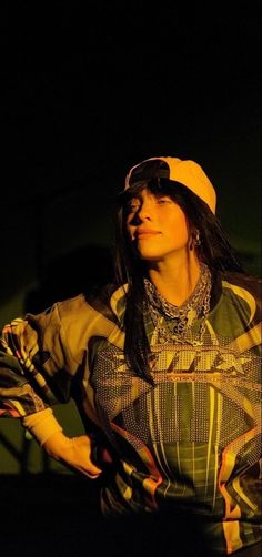 a woman with long hair wearing a yellow hat and green shirt standing in the dark