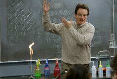 a man standing in front of a blackboard with writing on it and holding his hands up