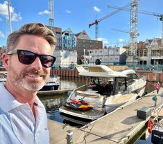 a man wearing sunglasses standing in front of a boat docked at a dock with other boats