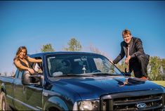 two people standing on the hood of a pickup truck with their hands in the bed