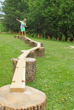 a young boy standing on top of a wooden bench made out of tree stumps