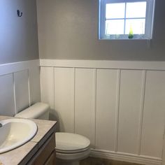 a white toilet sitting next to a sink in a bathroom under a window with wooden paneling