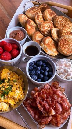 a breakfast tray with pancakes, berries, eggs, bacon, and other food items