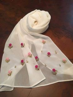 a white scarf with pink flowers on it sitting on top of a wooden table next to a pair of scissors