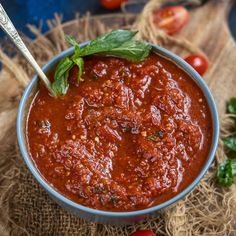 a bowl of tomato sauce with basil leaves and tomatoes around it on a burloom cloth