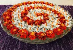 an orange and white flower arrangement in a glass platter on a purple tablecloth