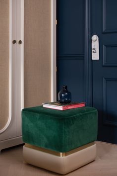 a green velvet stool in front of a blue door with two books on it and a vase next to it