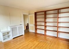 an empty room with wooden floors and white bookcases on the wall, next to a radiator