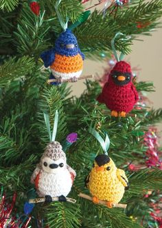 crocheted christmas ornaments hanging from a tree with pine needles and red, white, blue and yellow birds on them