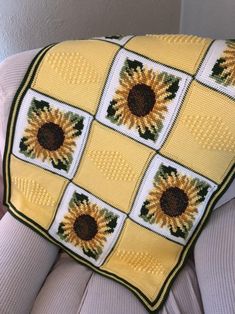 a crocheted sunflower blanket is on the back of a chair with a stuffed teddy bear