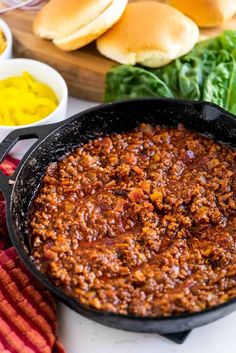 chili in a skillet next to buns and other condiments