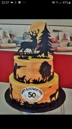 a three tiered cake decorated with deer and trees on it's side, sitting on top of a table