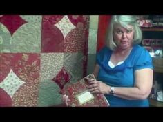 a woman holding a piece of fabric in front of a red and white quilted wall