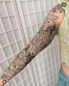 a woman's arm with flowers and leaves tattooed on her arm, next to a tiled wall