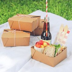 three boxes with food and drinks on a table outside in the grass, one has a straw