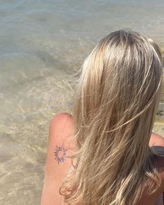 the back of a woman's head with a sun tattoo on her left shoulder