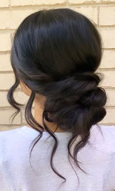 a woman with dark hair wearing a white shirt and braided up into a low bun