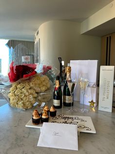 a table topped with bottles of wine next to champagne glasses and flowers on top of a marble counter