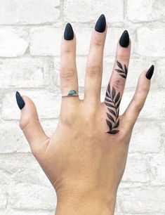 a woman's hand with black nail polish and tattoos on her left thumb, showing the ring finger tattoo design