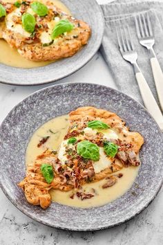 two plates topped with chicken covered in gravy and garnished with green leaves