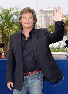 a man in a suit waves to the crowd while standing on a blue carpeted area