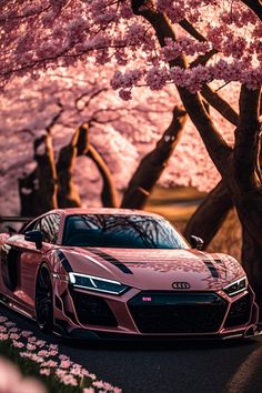 a pink sports car parked in front of cherry blossom trees with the sun shining on them