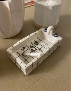 two white vases sitting on top of a table next to a tray with something in it