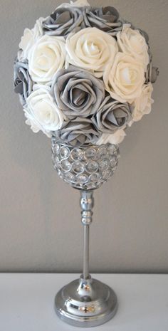 a silver vase filled with white roses on top of a table next to a wall