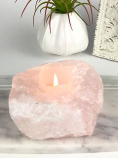 a pink candle sitting on top of a table next to a white vase filled with flowers