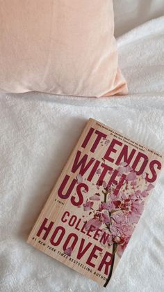 a book laying on top of a bed next to a pink pillow and white sheets