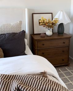 a bedroom with a bed, nightstand and flowers on top of the night stand in front of it