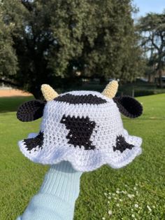 a crocheted cow hat is held in the air by someone's hand