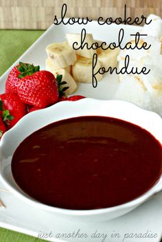 a bowl of chocolate fondue next to sliced bananas and strawberries on a plate