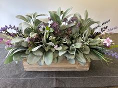 a wooden box filled with lots of different types of flowers and greenery on top of a table