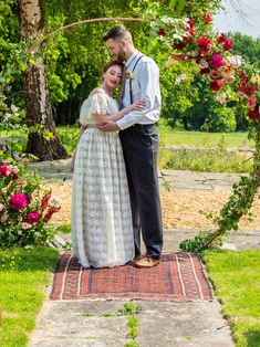 a man and woman standing in front of a floral arch with flowers on the ground