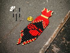 a red and black beaded brooch sitting on the ground next to a pin