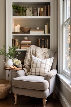 a white chair sitting in front of a window next to a book shelf filled with books