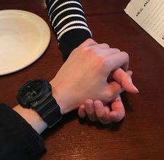 two people holding hands at a table with a book and plate on the table behind them