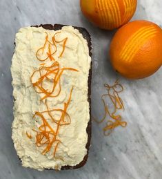 two oranges sitting next to a piece of bread with icing on it and an orange