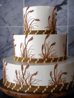 a three tiered white cake with brown designs on it's sides and gold trimmings