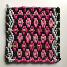 a pink and black crocheted square on a white surface with two rows of squares in the middle