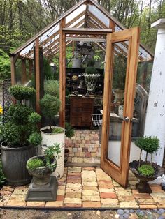 an outdoor garden with potted plants and a greenhouse in the back ground, surrounded by stone pavers