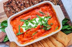 a casserole dish filled with tomato sauce, cheese and herbs on top of crackers